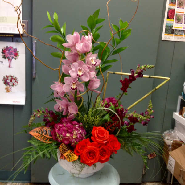 Tall floral arrangement with pink orchids and red roses in a white bowl