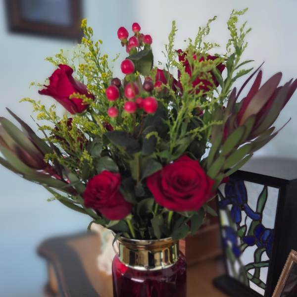 Red roses and berry stems arranged in a glass vase