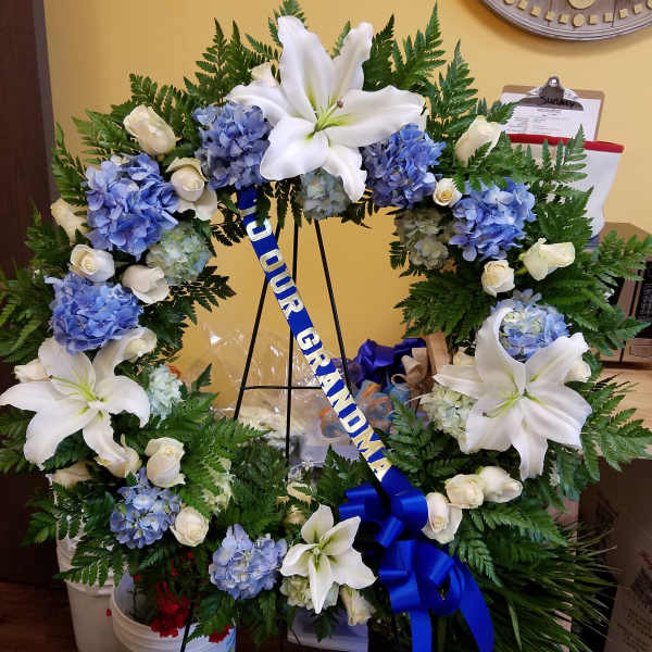 Floral graduation wreath with white lilies, blue hydrangeas, and roses on a stand