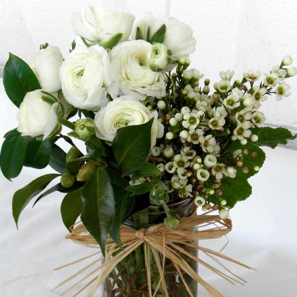 White ranunculus bouquet in a glass vase with a raffia bow
