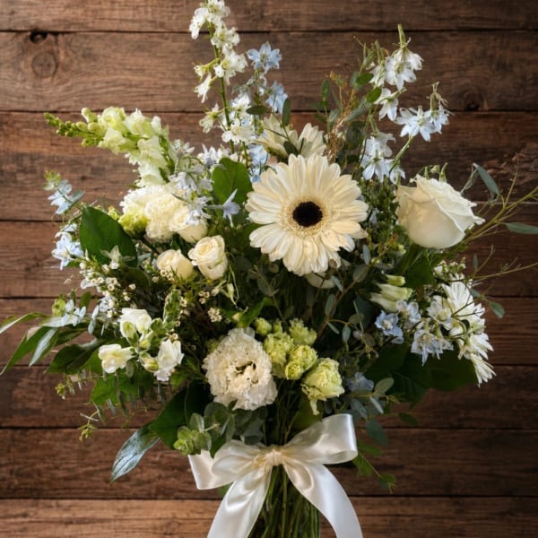 White and pale blue floral bouquet in a glass vase with a satin ribbon