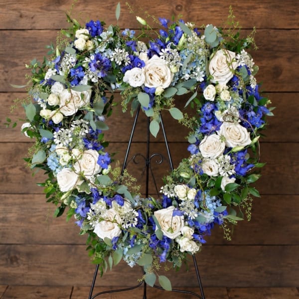 Heart-shaped floral wreath with white and blue flowers on a black stand
