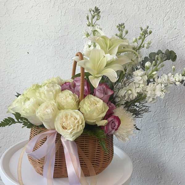 Basket arrangement of cream lilies, roses, and pink blooms with ribbon