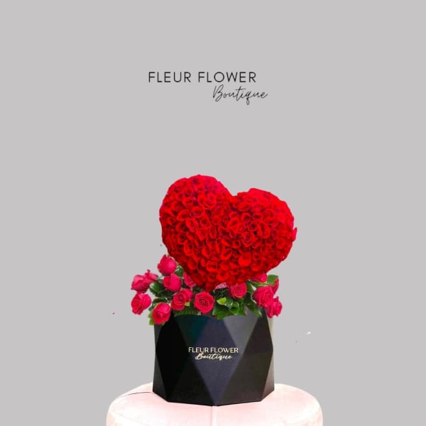 Heart-shaped red rose arrangement in a black box with pink roses around it