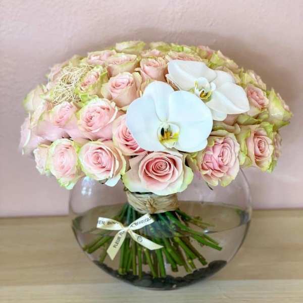 Pink roses and white orchids arranged in a round glass vase