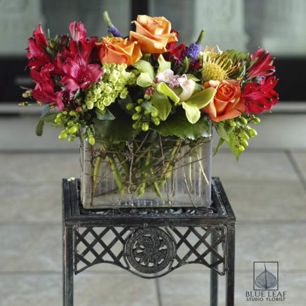 Colorful bouquet of orange roses and red flowers in a glass vase