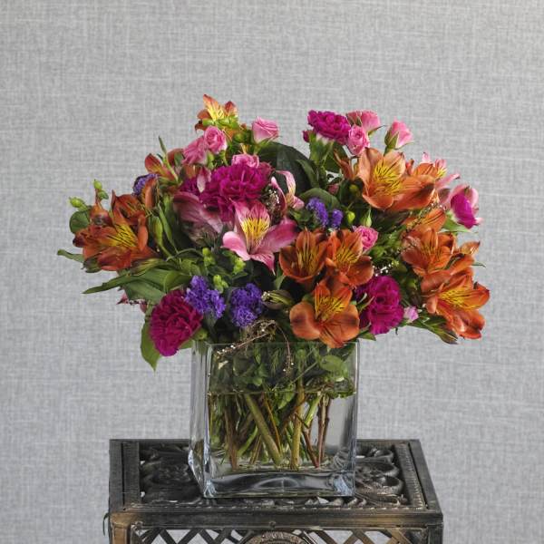 Colorful bouquet of orange, pink, and purple flowers in a clear glass vase