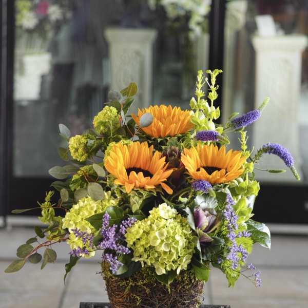 Orange sunflowers and purple accents in a woven basket arrangement