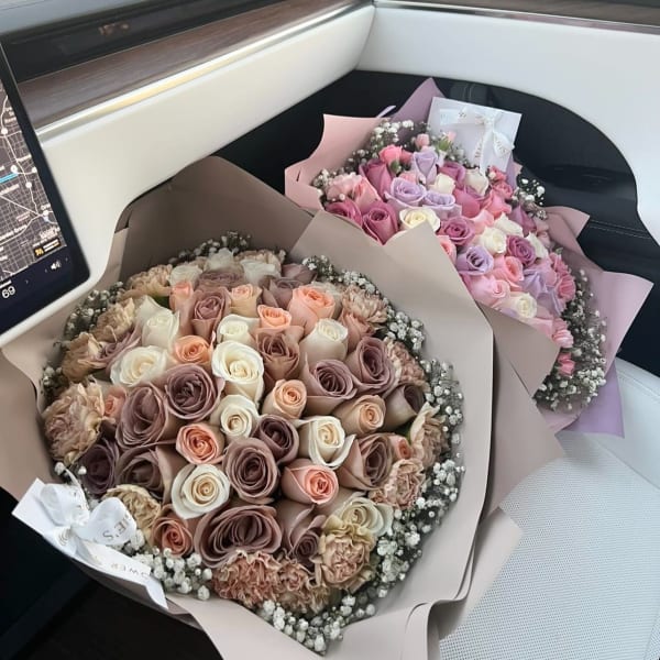 Two bouquets of pastel roses wrapped in paper on a car seat