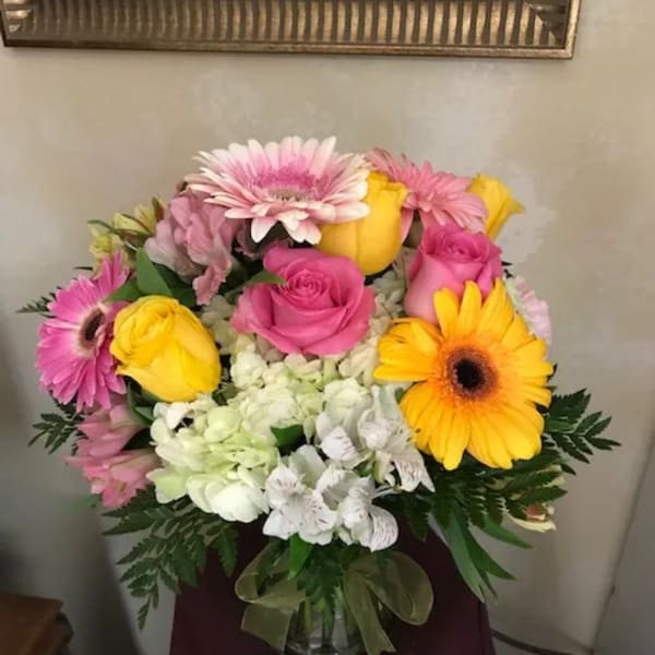 Pink and yellow roses with gerbera daisies in a glass vase