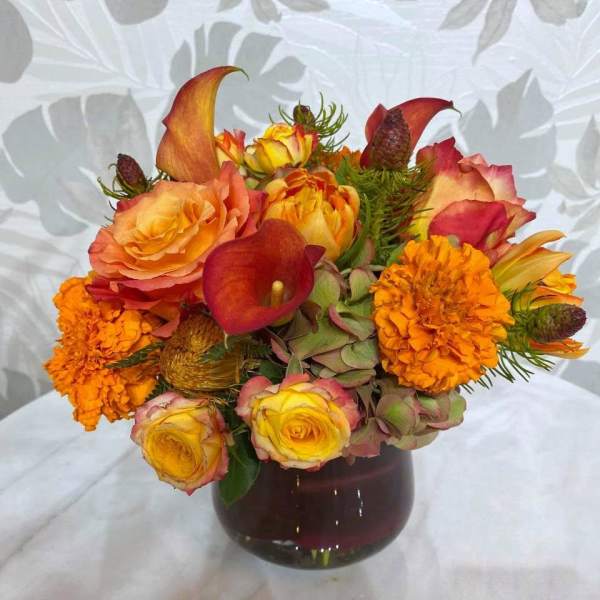 Orange and yellow roses with calla lilies and marigolds in a dark glass vase