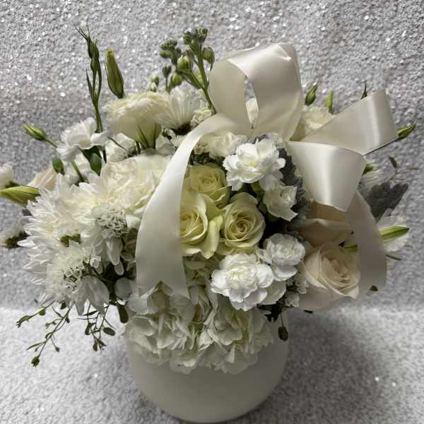 White floral arrangement with roses, carnations, and a satin ribbon in a vase