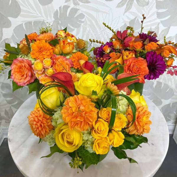 Three colorful floral arrangements with roses and dahlias on a round table