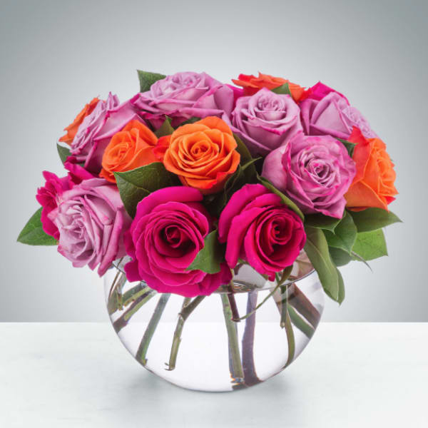 Mixed pink, lavender, and orange roses in a clear round vase