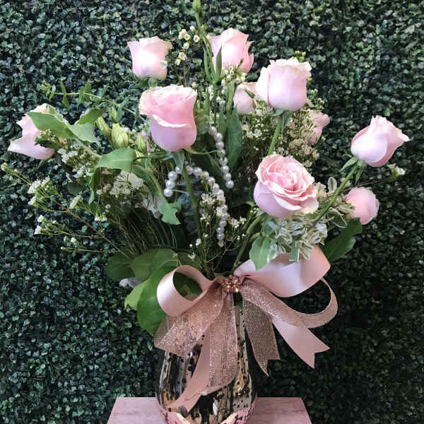 Pink roses arranged in a patterned vase with a pink ribbon bow