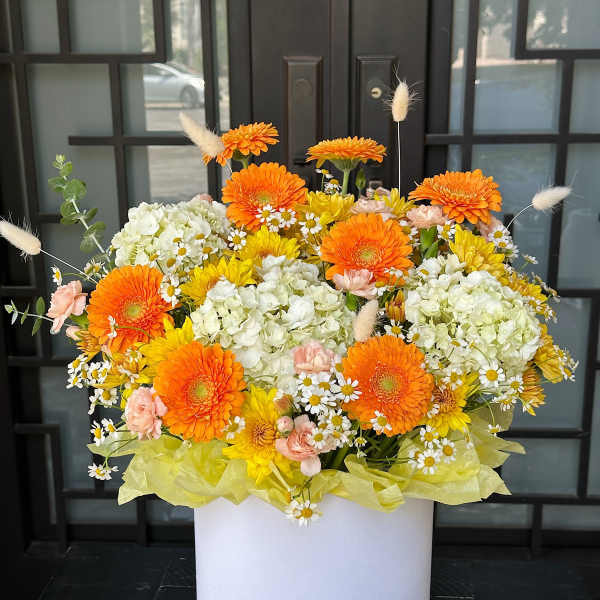 Bright mixed flower arrangement in a white box with orange and yellow blooms