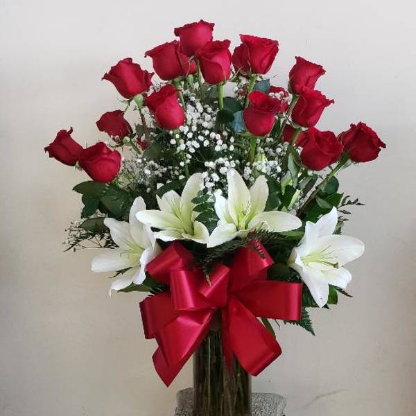Red roses and white lilies arranged in a tall glass vase with a red bow.
