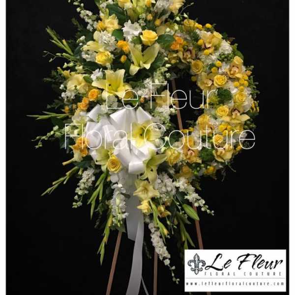 Yellow and white floral funeral wreath on an easel with a white ribbon