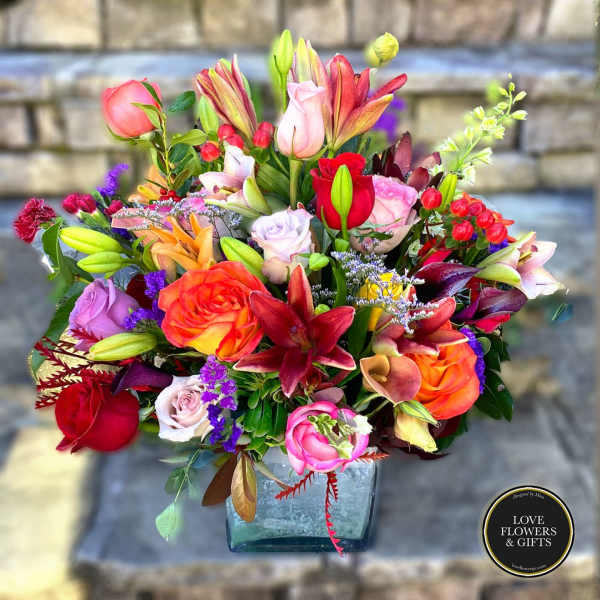 Vibrant mixed bouquet of roses and lilies in a square glass vase