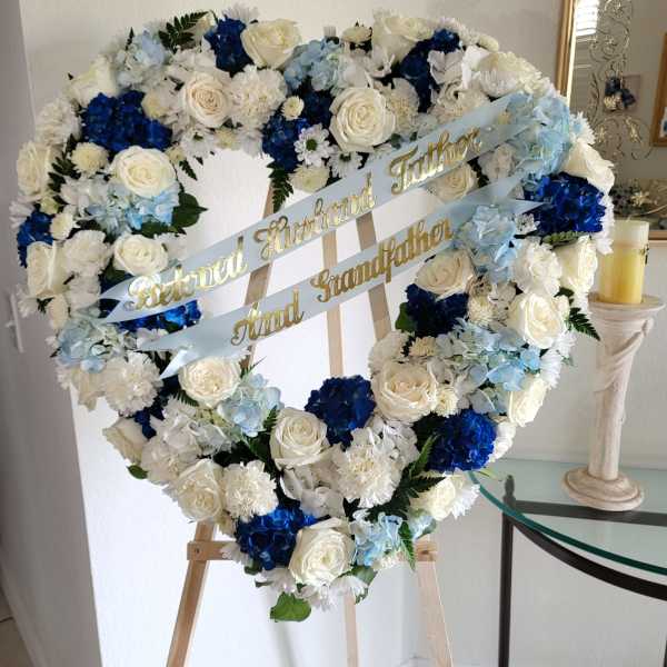 Heart-shaped floral wreath with white, blue, and pale blue flowers on an easel