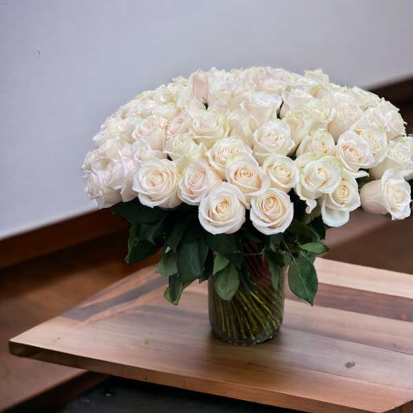 Large arrangement of cream roses tightly clustered in a clear glass vase on a wooden table