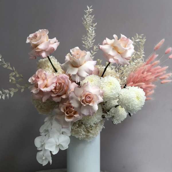 Pink roses and white pompom flowers in a tall white vase