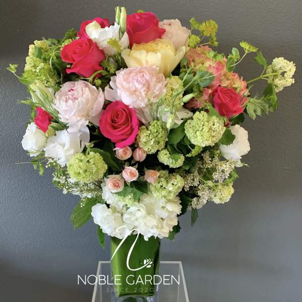 Mixed bouquet of pink, white, and green flowers in a tall glass vase