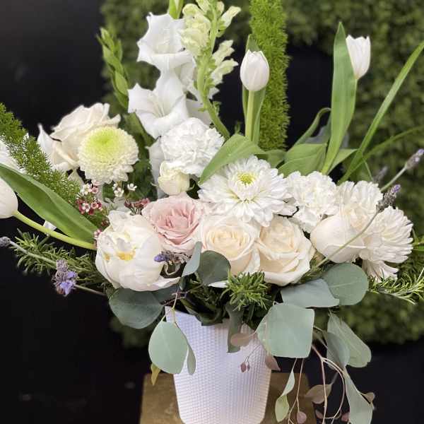 White floral arrangement in a textured vase with tulips and roses