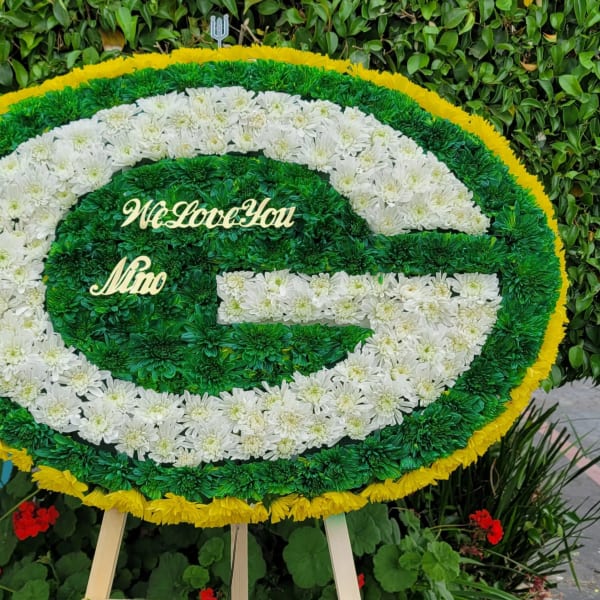 Oval floral tribute in green, white, and yellow with a message in the center