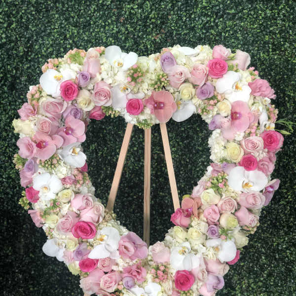 Heart-shaped floral wreath of pink, white, and lavender blooms on a wooden stand