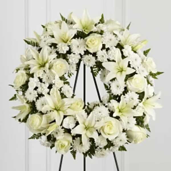 White floral wreath with lilies and roses on a black easel