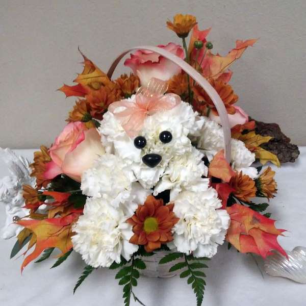 Basket arrangement with white flowers, orange blooms, and a teddy bear face