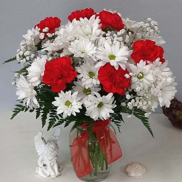 Red carnations and white daisies in a glass vase with a red ribbon