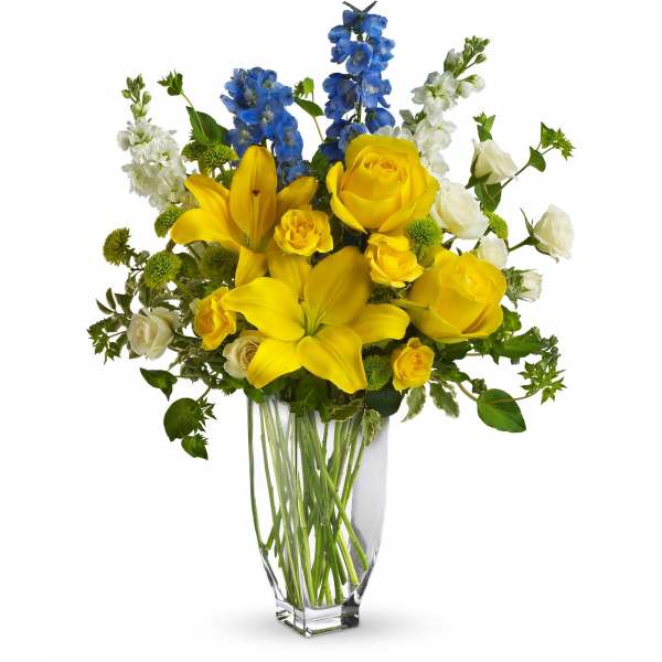 Yellow roses and lilies with blue and white flowers in a clear vase