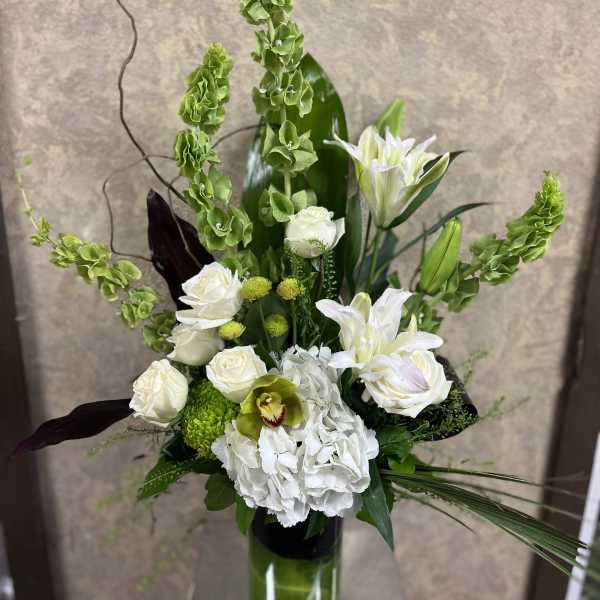 Tall white and green floral arrangement in a glass vase