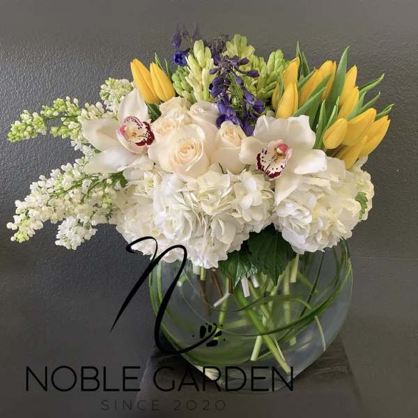 Mixed bouquet of white, yellow, and purple flowers in a glass vase