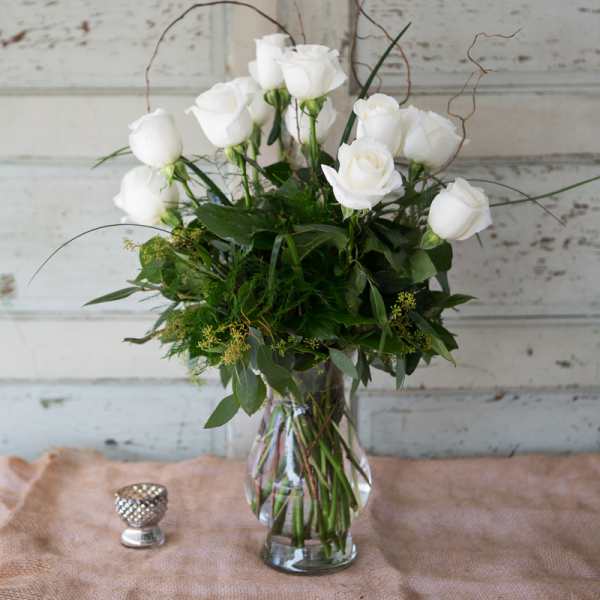 White roses in a clear glass vase with greenery