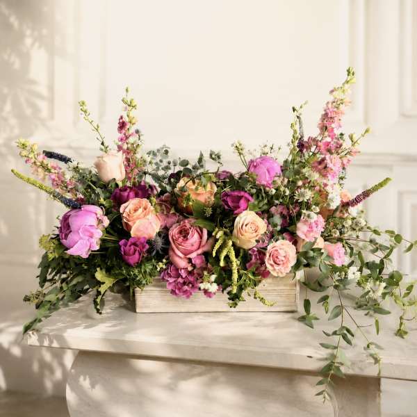 Low floral arrangement of pink and peach roses in a wooden box