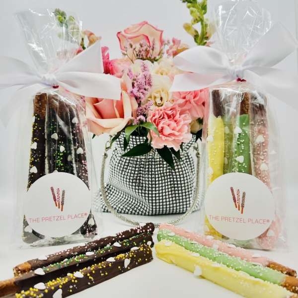 Flower arrangement with pink and peach roses beside wrapped chocolate-covered pretzels
