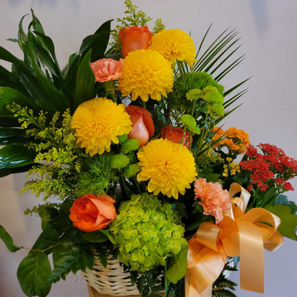 Basket arrangement with yellow mums, orange roses, and green hydrangea