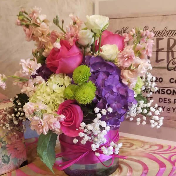 Pink, purple, and white flower arrangement in a round vase with a pink ribbon