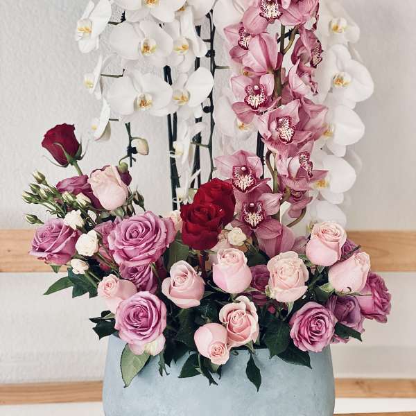 Pink and white orchids with roses in a round blue vase