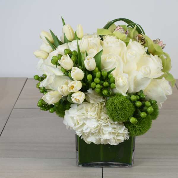 White floral arrangement in a green glass vase with green accents