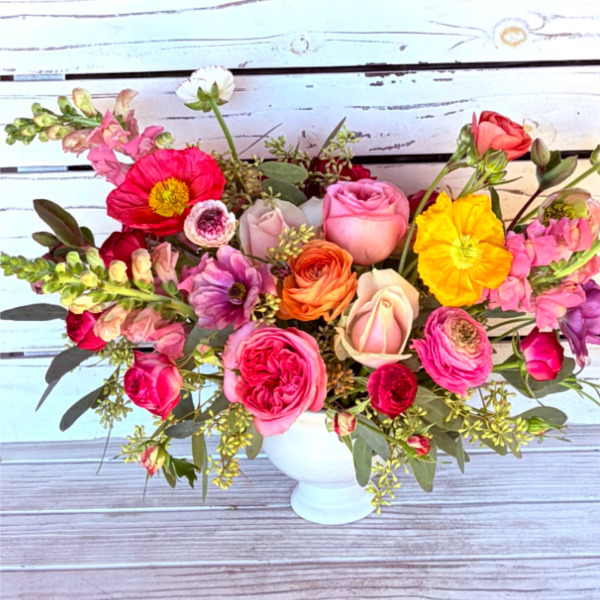 Colorful arrangement of roses, ranunculus, poppies, and snapdragons in a white pedestal vase