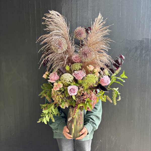 Tall bouquet of pink roses and dried grasses in a glass vase