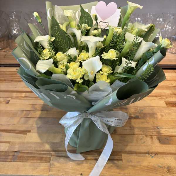Bouquet of white calla lilies and yellow spray roses wrapped in green paper