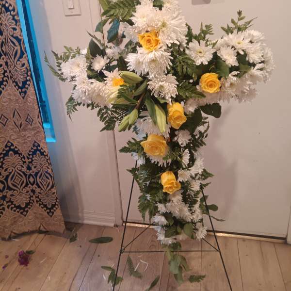 Cross-shaped floral spray with white daisies and yellow roses on a stand