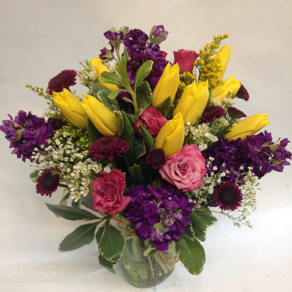 Bouquet of yellow tulips, pink roses, and purple flowers in a glass vase