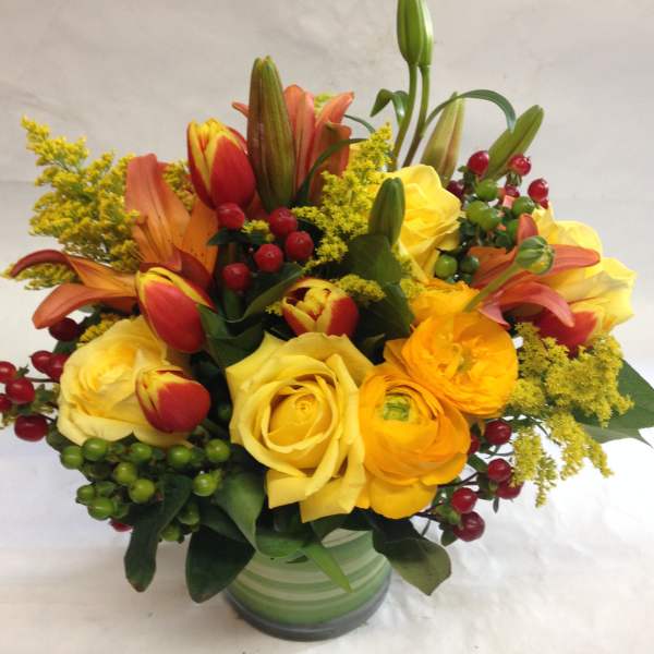 Bouquet of yellow roses, tulips, and lilies in a green striped vase