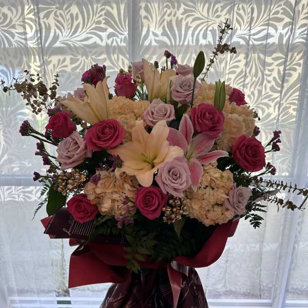 Large bouquet of pink roses, lilies, and hydrangeas in burgundy wrap